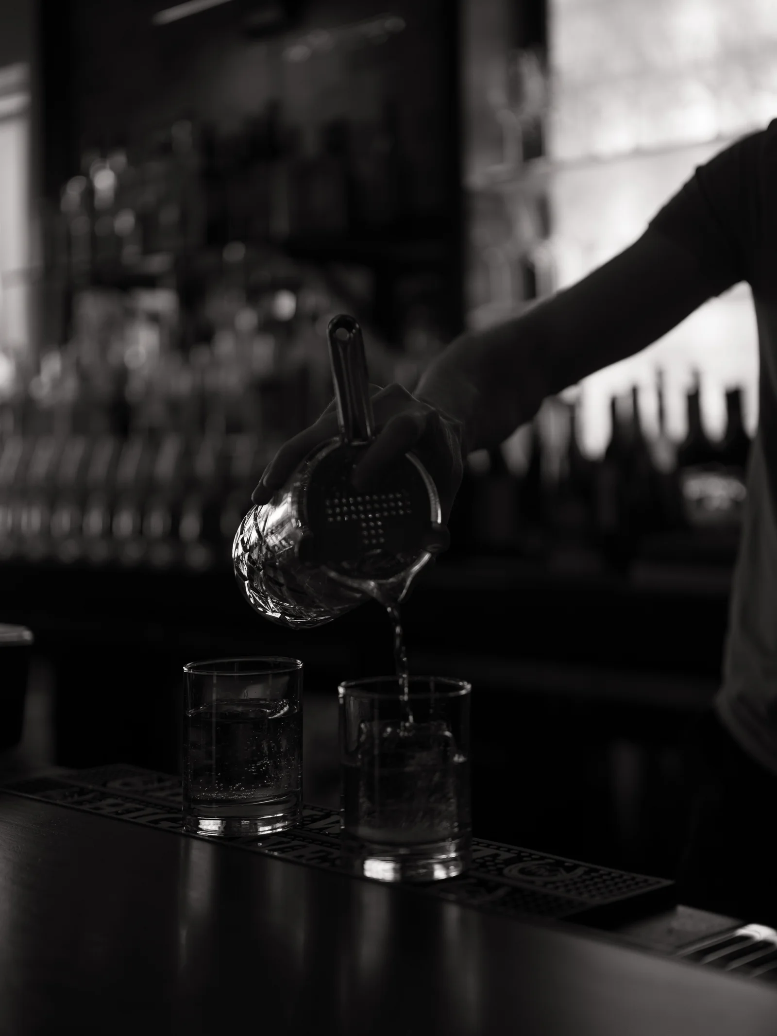 A bartender pouring cocktails through a strainer in black and white